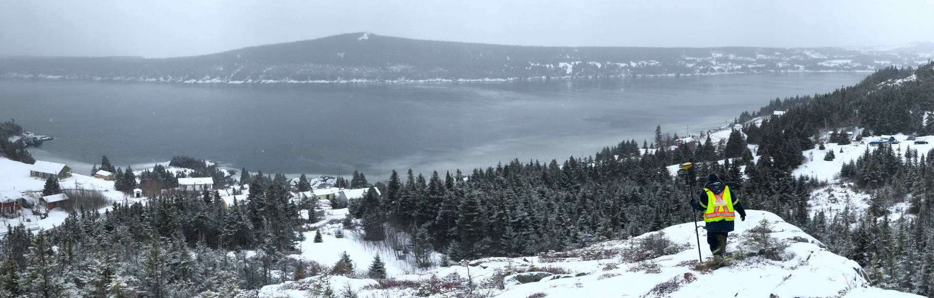 Snow-capped hill over the water with surveyor atop.